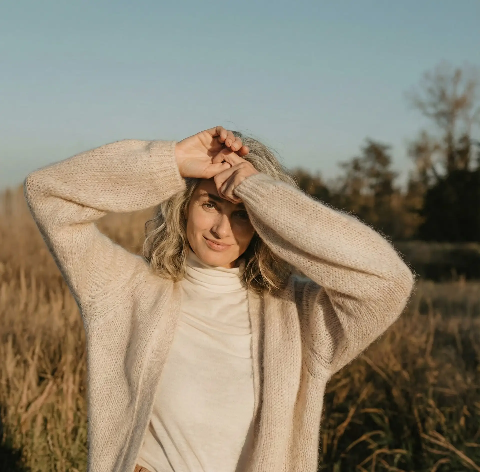 Vrouw in een zonnig veld in een crèmekleurig vest, vol vitaliteit