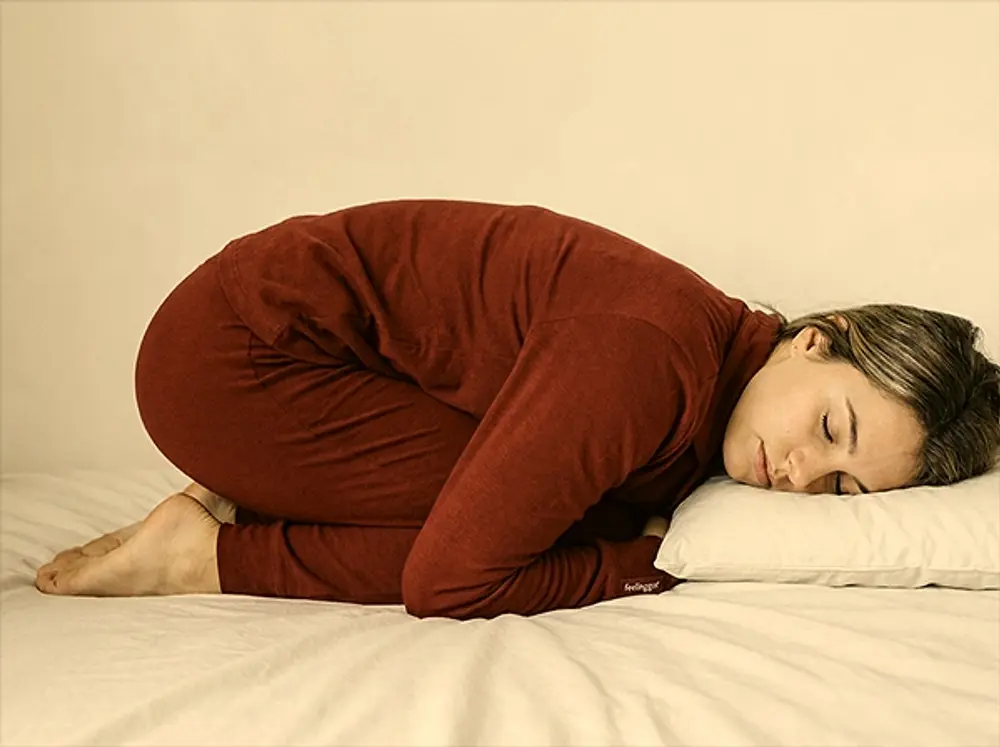 Vrouw ligt opgekruld op bed in warm licht, uitgeput maar in rust